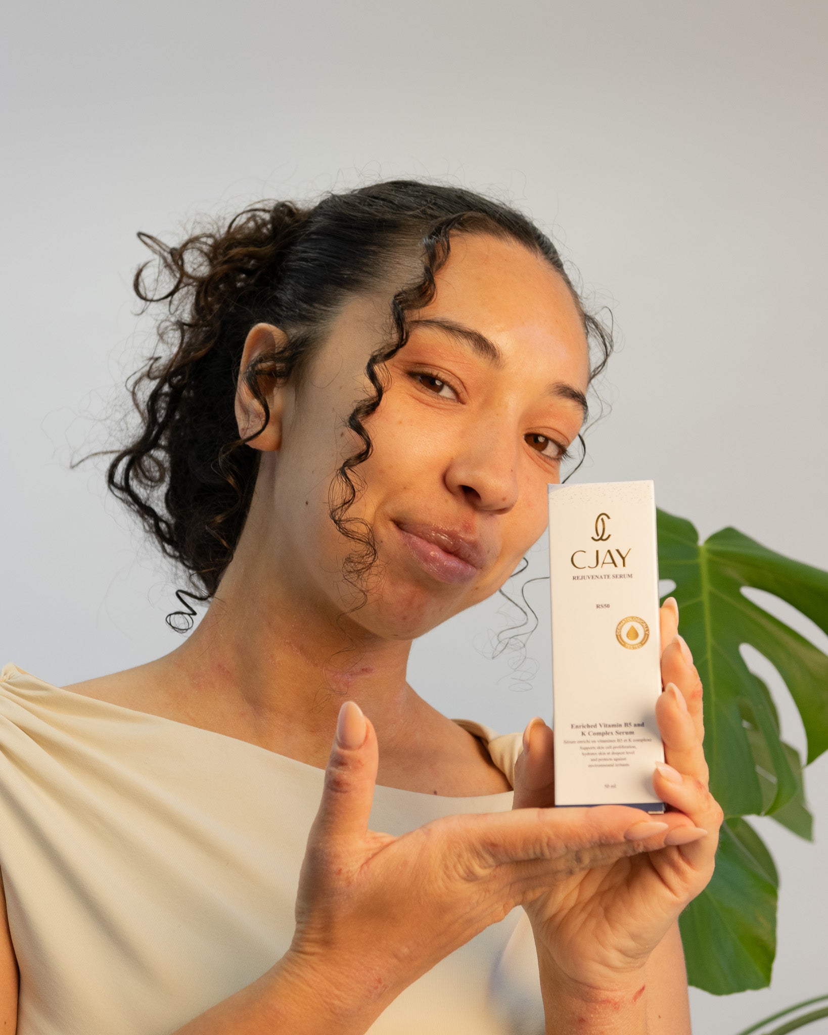 Woman holding a CJAY skincare product with a green leaf in the background