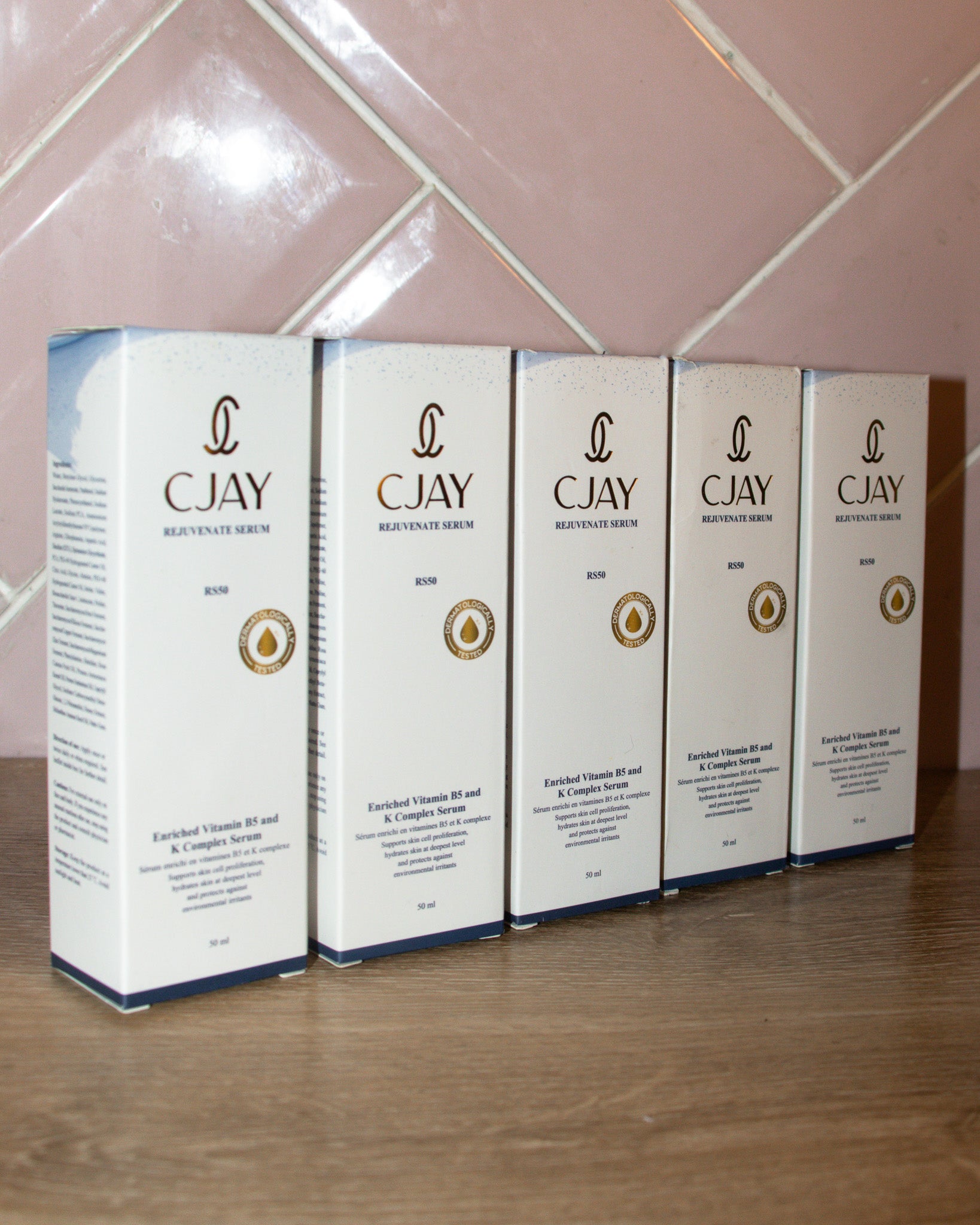 Five boxes of CJAY skincare serum on a wooden surface with a tiled wall background.